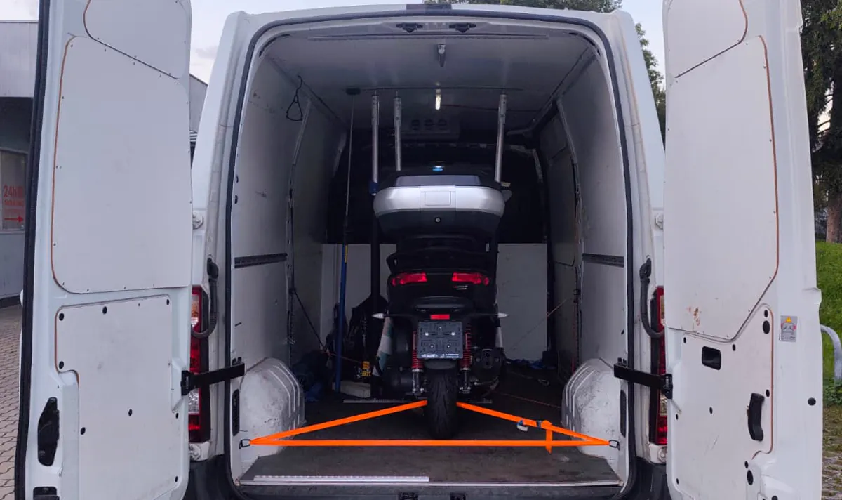 A motorbike inside a van's load area, secured with orange tie-down straps